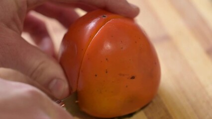 Poster - Cutting persimmon in half on wooden table. Eating tasty and juicy date-plum