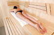 © Nobilior - Woman relaxing in a sauna. She is lying on a towel.