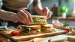 Close-up of hands placing a sandwich on a wooden cutting board in a kitchen setting