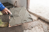 Fototapeta Zachód słońca - Hand tiler plastering cement glue with trowel on tile installing floor project, Real action worker in construction site