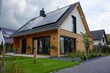 Modern suburban passive house with photovoltaic system on gable roof, driveway, and landscaped yard