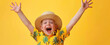 A young boy dressed in summer attire, wearing yellow shirt and straw hat with closed eyes is making peace sign while laughing out loud against vibrant yellow background.