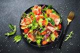 Fototapeta  - Healthy food. Fresh salad with jamon, green salad leaves and tomatoes. Top view with space for text.