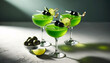 Three vibrant green cocktails in classic coupe glasses, each adorned with a skewer of black olives and a zest of lime. The drinks are set on a light