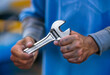 A man's hand holding a large wrench in front of a mechanic's garage	
