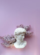 Plaster head of David and violet lilac flowers on pink background. floral composition with antique statue head. spring season. modern style for man beauty. creative art concept. flat lay. copy space