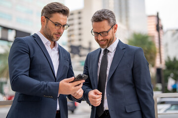 Wall Mural - Planning of the two business mens strategy. The two business mens strategic. Goal helped the two business men stay success. Business mens strategy. Two businessmen using phone outdoor.