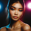 Young female asian model with stylish eyes makeup and shadows on face standing in studio illuminated with colorful spotlights
