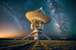Radio telescope is in the middle of a field at night. The sky is filled with stars and the Milky Way