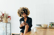 © VICTOR TORRES/Stocksy - Young afro woman using smartphone in a modern kitchen