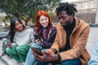 © Lomb - Multicultural friends trio enjoys a moment of urban camaraderie - young adults sharing interesting content on smartphones - intersection of technology and social interactions - city setting.