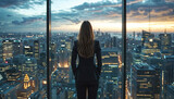 Fototapeta Sport - Person in office space, overlooking a stunning cityscape at dusk. Urban skyline is adorned with illuminated high rise buildings under a cloudy sunset, all reflected in the window glass.