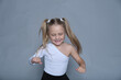 Joyful little girl dancing in a white top, her hair in playful pigtails, embodying happiness and carefree childhood moments.