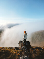 Wall Mural - Woman standing on mountain cliff edge above clouds in Norway, traveler hiking solo outdoor active healthy lifestyle adventure summer vacations harmony with nature