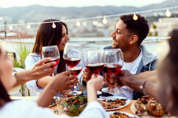 Wall Mural - Group of people enjoying summer night dinner party at home terrace. Multiracial friends social gathering reunited together celebrating at rooftop. Summertime concept.