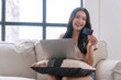 © kaew6566 - Enjoy asian woman showing credit card payment shopping online with laptop sitting on sofa. Cheerful Asia young girl holding card mockup smile relax pay on internet at apartment. Technology pay concept