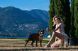 Girl play with Boxer dog near nature with mountain background. Girl throwing ball to boxer dog. Dog tries to catch ball. Sensual Woman playing with dog in park on summer day. Lovely pet.