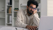 © Yuliia - Arabian Indian ethnic male tired businessman office employee boring work with laptop dreary exhausted lazy bored business man low energy overworked fatigue depression apathy burnout typing on computer