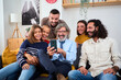 © CarlosBarquero - Caucasian multi-generational family gathered at living room sitting on sofa using mobile phone. Happy people smiling with a fun expression enjoying and watching funny videos together in cell at home