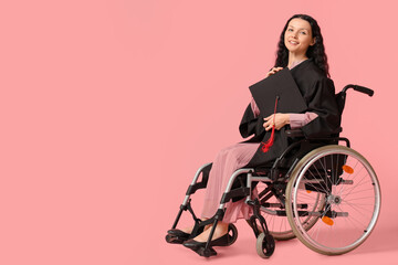 Beautiful female graduate student in wheelchair with graduation cap on pink background