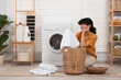 © New Africa - Happy woman with laundry near washing machine indoors