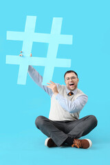 Wall Mural - Male office worker with hashtag sitting on blue background