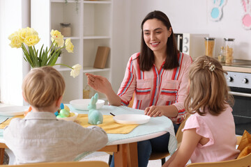 Wall Mural - Happy mother with her little children having Easter dinner in kitchen