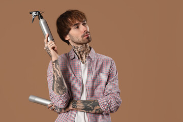 Poster - Thoughtful tattooed barber with hair sprays on brown background