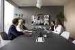 Group of businesspeople gathered in conference room take part in virtual meeting with international corporate partners using video call apps, engaged in online remote negotiations or briefing event