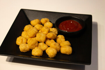 Crispy chicken popcorn with tomato ketchup in a black ceramic plate