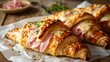 Croissant with ham and brie cheese on white parchment.