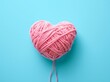 A pink ball of yarn shaped like a heart on a blue background conveys passion for knitting and the warmth of handmade creations in summer