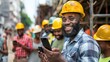 A man with a beard and a yellow hard hat is smiling and holding a cell phone