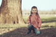 Kleine hübsches Mädchen kniet auf einer Wiese an einem Baum im Frühling, outdoor
