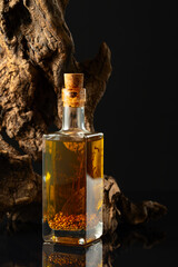 Canvas Print - Bottle of spicy oil and olive tree snag on a black background.