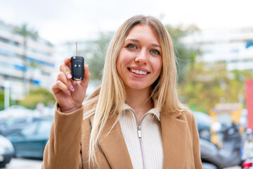 Wall Mural - Young pretty blonde woman holding car keys at outdoors smiling a lot