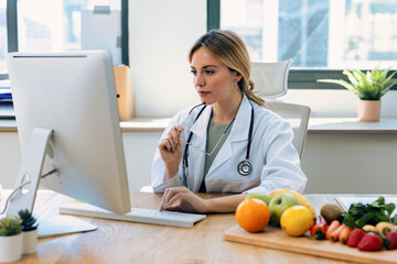 Beautiful smart nutritionist woman working with computer while taking notes in the nutritionist consultation