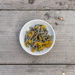 White bowl with  dried coltsfoot on a wooden background