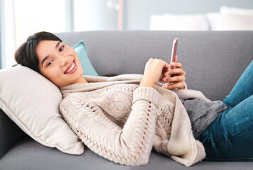 Poster - Asian woman, home and smile on sofa with smartphone, text and messages with dating app and social media. Female person, internet and online for post, content update and happy with videos in portrait