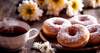 A close-up of a plate of donuts, lightly dusted with sugar, sits on an old wooden table next to a cup of tea