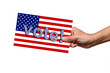 The female hand holding a flyer with an American flag and the slogan Vote! calling for participation in the presidential election isolated on a white background. Poll, ballot, competition, politics