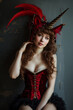 Unicorn Woman with Bare Shoulders, Long Chestnut Hair, and Red Mask with Unicorn Horn and Feathers in a Red Velvet Corset Dress with a Graphite Muslin Finish Running Around the Bottom