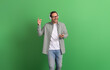 Happy young man snapping fingers and singing while listening music over headset on green background