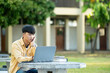 Pensive Student with Laptop Outdoors on University Grounds