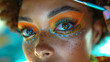 Close-up of a young woman with creative makeup, featuring orange eyeshadow, long eyelashes, and decorative face art, with a makeup brush applying product near her eye.