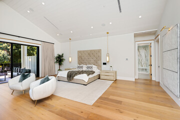 this bedroom has white walls and wood flooring, a bed with two armchairs