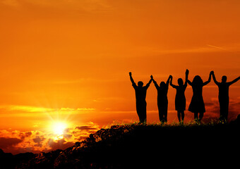 Wall Mural - group of silhoutted people on hill arms raised and holding hands over orange colored sunset sky