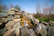 An artificial waterfall with flowing water and stone structures. Authentic landscape overlooking a spring garden.