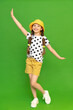 A little girl in a hat and shorts is enjoying the warm summer. Children's summer holidays.  The young girl opens her arms in different directions and smiles broadly. Green isolated background.