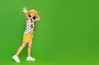 A child in summer clothes points to your ad. A young girl in shorts and a hat is enjoying her summer vacation. Children's holidays. Green isolated background. Copy space. Place for the text, banner